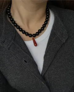 Close-up of vintage oil painting style necklace with black beads and red teardrop pendant