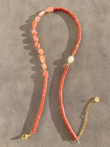 Detail of beaded necklace featuring orange natural stones and gold metal lobster clasp