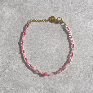 Detail of beaded bracelet with red glass beads, freshwater pearl, and gold heart charm