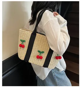Stroh-Stofftasche mit Kirsch-Pompons am Modell für einen lässigen Urlaubs-Look