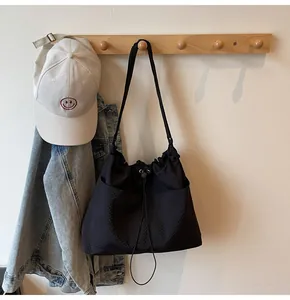 Detail of black pleated nylon tote bag with drawstring closure and side pocket on a wall hook