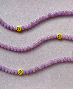 Detalle de cuentas de calcedonia púrpura con caritas amarillas y cordón naranja