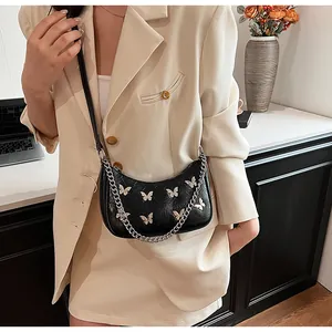 Detail of black crossbody bag with golden butterfly accents and silver chain link