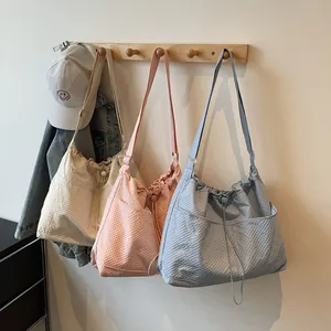 Three pleated canvas tote bags in white pink and blue colors on a wooden hanger