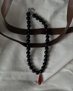 Retro beaded necklace with black round beads and red teardrop pendant on white canvas