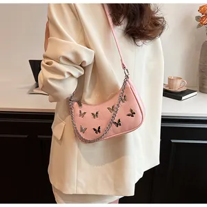 Detail of pink half-moon underarm bag with metal butterfly charms and chain strap