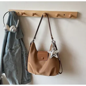 Brown leather crescent shoulder bag with a silver star charm on a wooden wall hook