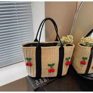 Detail der beigen Strohtasche mit 3D-Kirsch-Applikationen und schwarzen Stoffgriffen