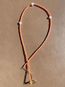 Detailed close-up of orange beads and freshwater pearls with gold heart pendant