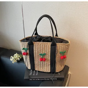 Detail der Strohtasche mit Häkelkirschen-Anhängern und schwarzem Kordelzug-Futter