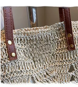Detailed view of woven straw tote with brown leather handles and brand logo patch