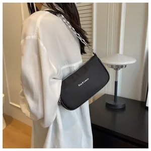 Detail of black nylon baguette bag with silver chain and white Rioa & Luxury text logo