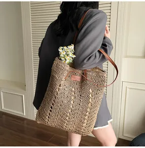 Detail of hand-woven straw tote bag with brown leather handles and brand logo tag