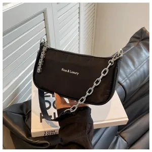Detail of black nylon baguette bag with silver chain and white logo on white books