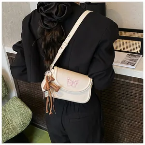 Gros plan du sac crème avec broderie papillon rose et breloque petit chien marron