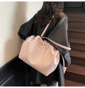 Detail of light pink patent leather bucket bag with bow shown on a shoulder