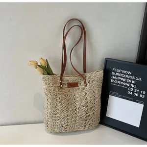 Detail of hand-woven straw tote bag with brown leather straps and branded logo label
