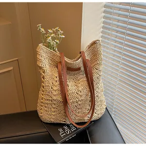 Detail of hollow crochet straw tote bag featuring brown leather handles and a brand label