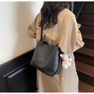 Detail of a black minimalist tote bag with a cute plush puppy charm on a camel coat model