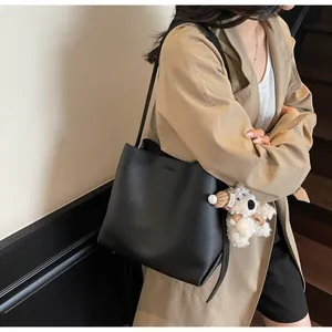Detail of black leather bucket bag with a cute brown plush bear charm and thin shoulder strap