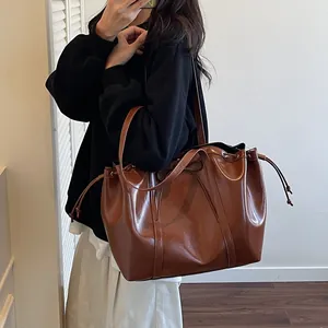Brown faux leather bucket bag with drawstring closure worn by model in a minimalist setting