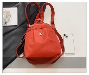 Detail of brick red nylon backpack featuring pleated fabric design and metal logo