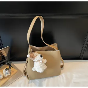 Detailed view of camel leather bucket bag with plush dog charm and adjustable strap