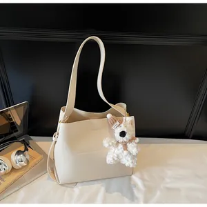 Detail of a creamy white leather tote bag with a plush bear charm and side pleats