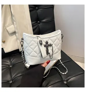 Detalle de bolso acolchado blanco con adornos de cruz gótica y colgante de calavera