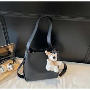 Chic black leather bucket bag with cute bear charm and wide strap on office desk