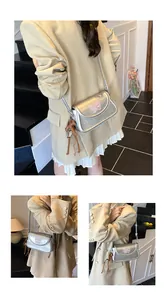 Détail du sac bandoulière argenté avec broderie papillon rose et breloque à pompon marron