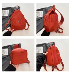 Detail view showing rust red mini nylon backpack with multiple zipper pockets and metal buckle