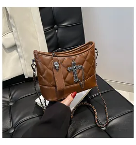 Detalle de bolso acolchado marrón con cruz plateada, cadenas y colgante de calavera