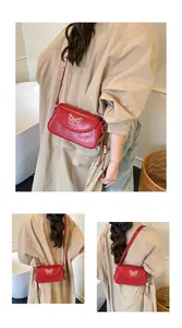 Détail du sac à bandoulière en similicuir rouge avec broderie papillon blanche et pompons en cuir