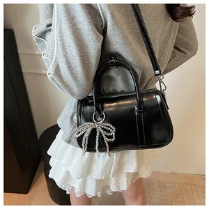 Detail einer glänzenden schwarzen Boston-Handtasche mit Perlen-Schleife und Schultergurt