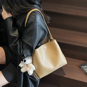 Minimalist beige matte leather bucket bag with cute plush bear charm on shoulder strap