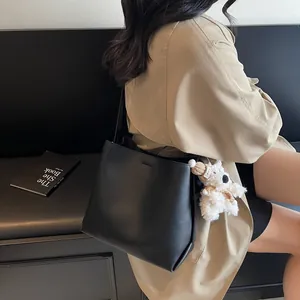 Minimalist black faux leather bucket bag with a cute plush bear pendant on model