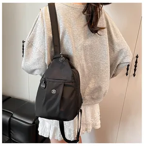 Detail of a chic black nylon mini backpack with M-logo and decorative pleats on a model