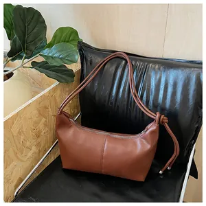 Close-up of brown leather shoulder bag featuring stylish knot detail and silver metal sphere