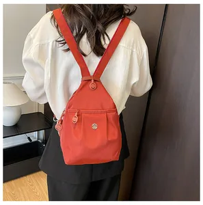 Detail of orange canvas backpack showing round metal M logo and high-quality zipper hardware