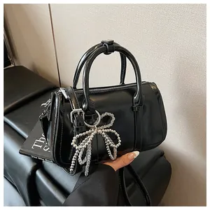 Detail der schwarzen glänzenden Boston-Tasche mit Perlen-Schleifen-Anhänger und Reißverschluss