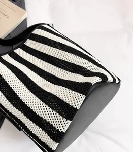 Detail van zwart-wit gestreepte mesh tas met gladde zwarte lederen zijpanelen