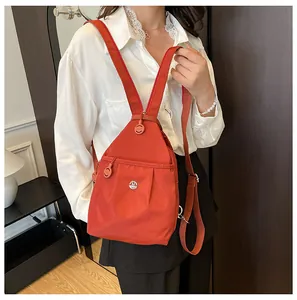 Detail of an orange-red nylon mini backpack with a metallic M logo and adjustable straps