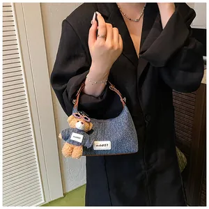 Details der blauen Denim-Halbmondtasche mit Lederriemen und Plüschbär-Anhänger