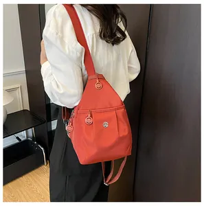 Close-up of brick red nylon backpack with round metal M logo and adjustable strap