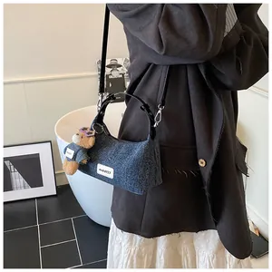 Detail der dunkelblauen Denim-Tasche mit weißem Logo und süßem Bären-Anhänger-Zubehör