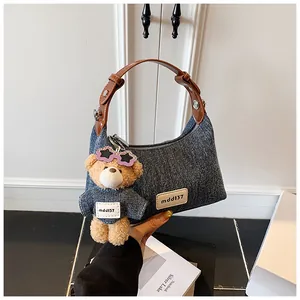 Detailansicht der Denim-Schultertasche mit Teddybär-Anhänger und Lederriemen-Akzenten