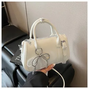Detail einer cremeweißen Boston Bag mit silbernem Perlenbogen-Anhänger und Lederstruktur