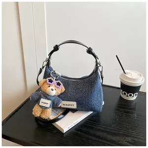 Detailansicht der Denim-Achseltasche mit Teddybär-Anhänger und Ledergriff auf Tisch