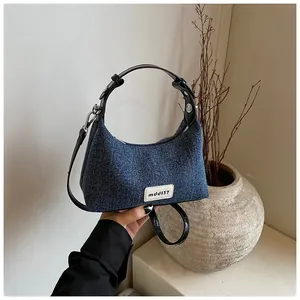 Nahaufnahme der sichelförmigen Denim-Tasche mit schwarzem Ledergriff und Silberreißverschluss